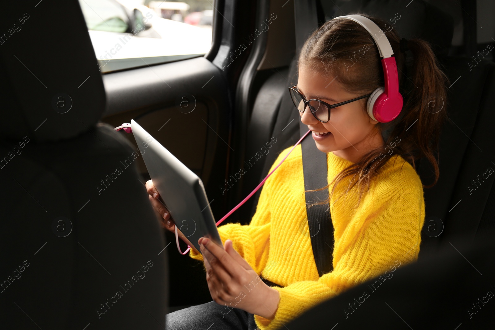 Photo of Cute little girl listening to audiobook in car