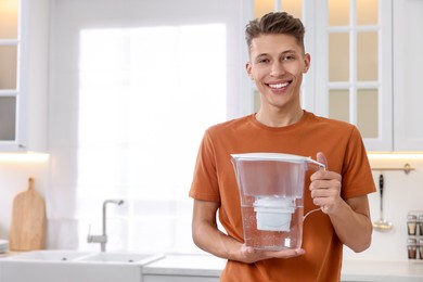 Photo of Happy man with water filter jug in kitchen. Space for text