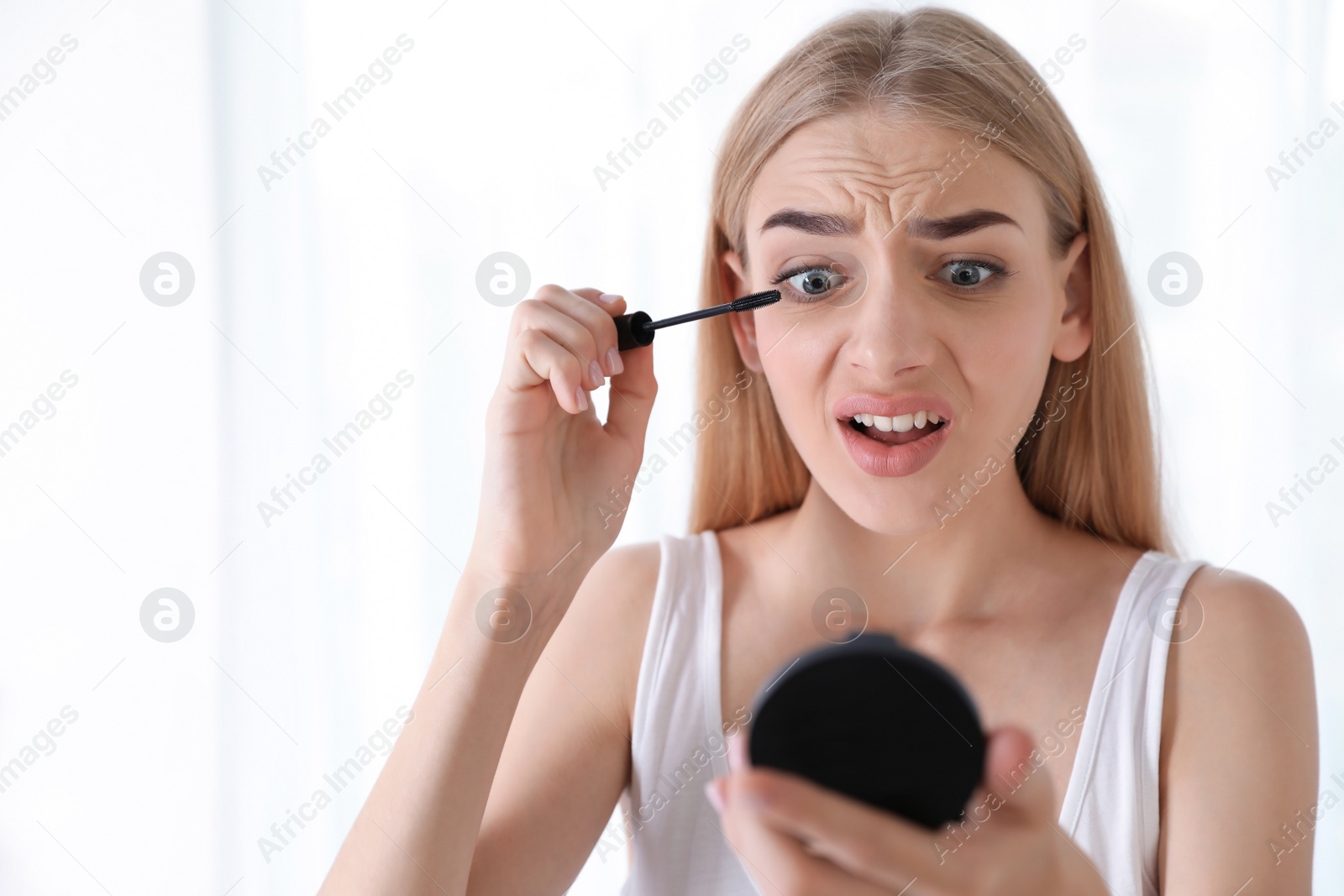 Photo of Emotional woman with eyelash loss problem applying mascara indoors