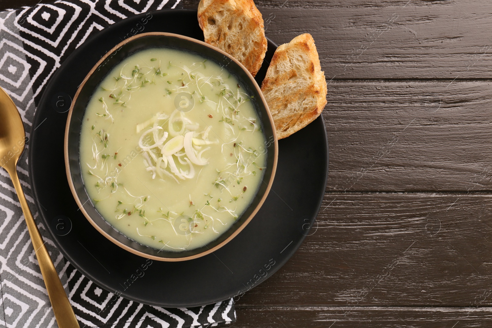 Photo of Delicious leek soup served on brown wooden table, top view. Space for text