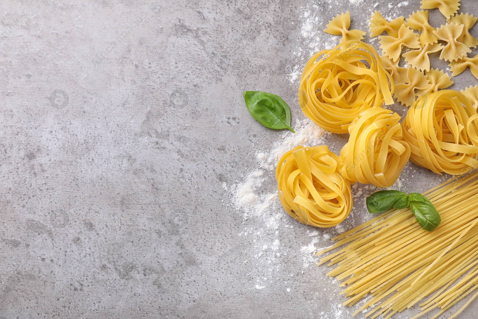 Photo of Flat lay composition with different types of pasta on grey background. Space for text