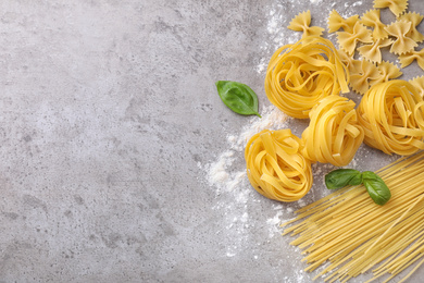 Photo of Flat lay composition with different types of pasta on grey background. Space for text