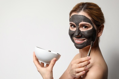Photo of Beautiful woman applying black mask onto face against light background. Space for text