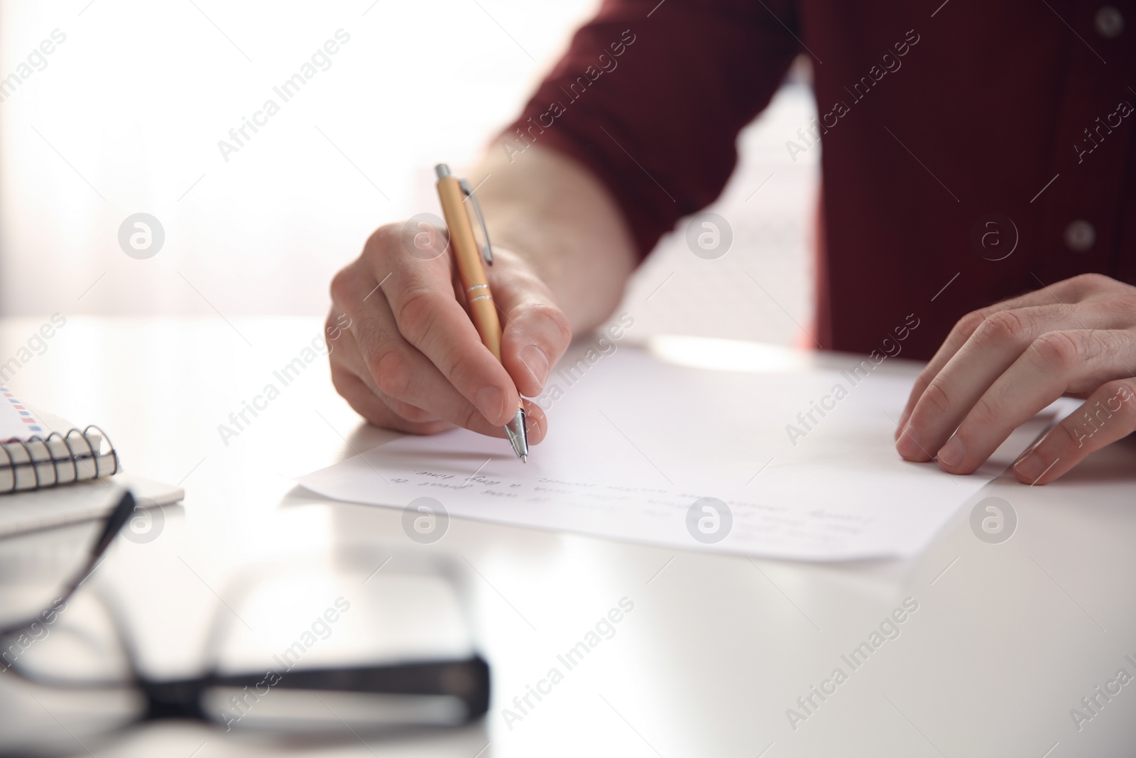 Photo of Man writing letter at white table, closeup