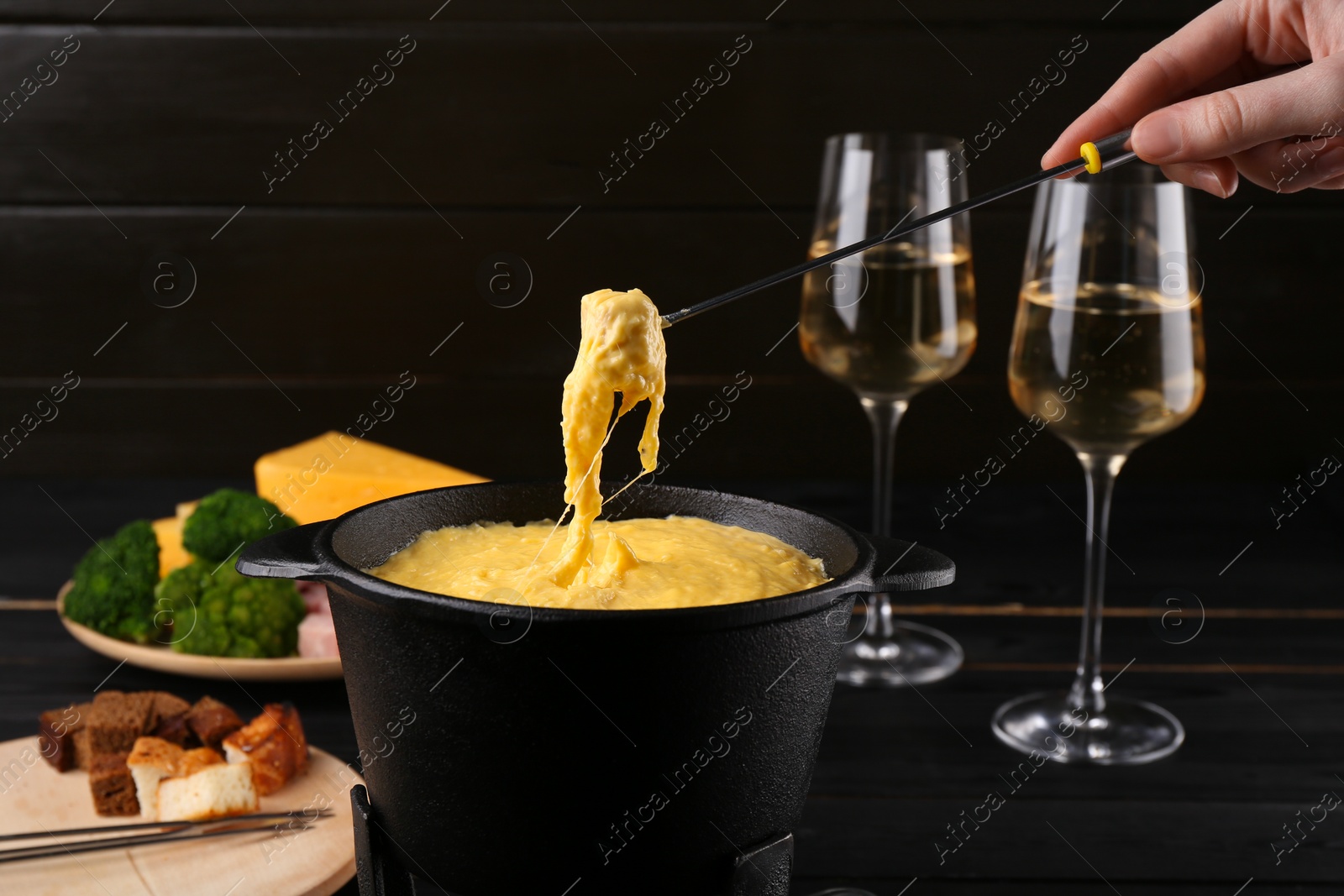 Photo of Woman dipping piece of ham into fondue pot with melted cheese at table, closeup