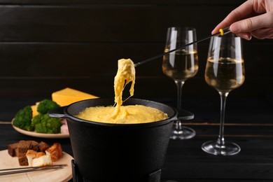 Photo of Woman dipping piece of ham into fondue pot with melted cheese at table, closeup