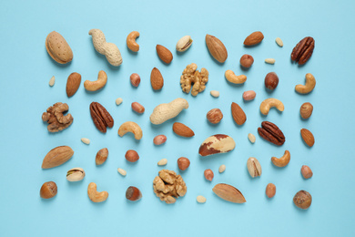 Different delicious nuts on light blue background, flat lay