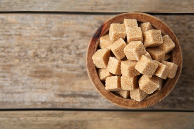 Photo of Bowl with brown sugar cubes on wooden table, top view. Space for text