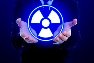 Man holding glowing radiation warning symbol on dark blue background, closeup