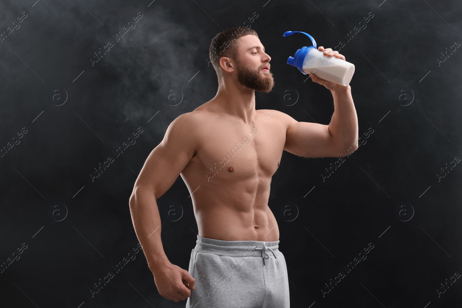 Photo of Young man with muscular body drinking protein shake on black background