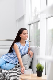 Young beautiful woman drinking morning coffee near window at home