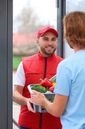 Photo of Courier giving plastic crate with products to customer at home. Food delivery service