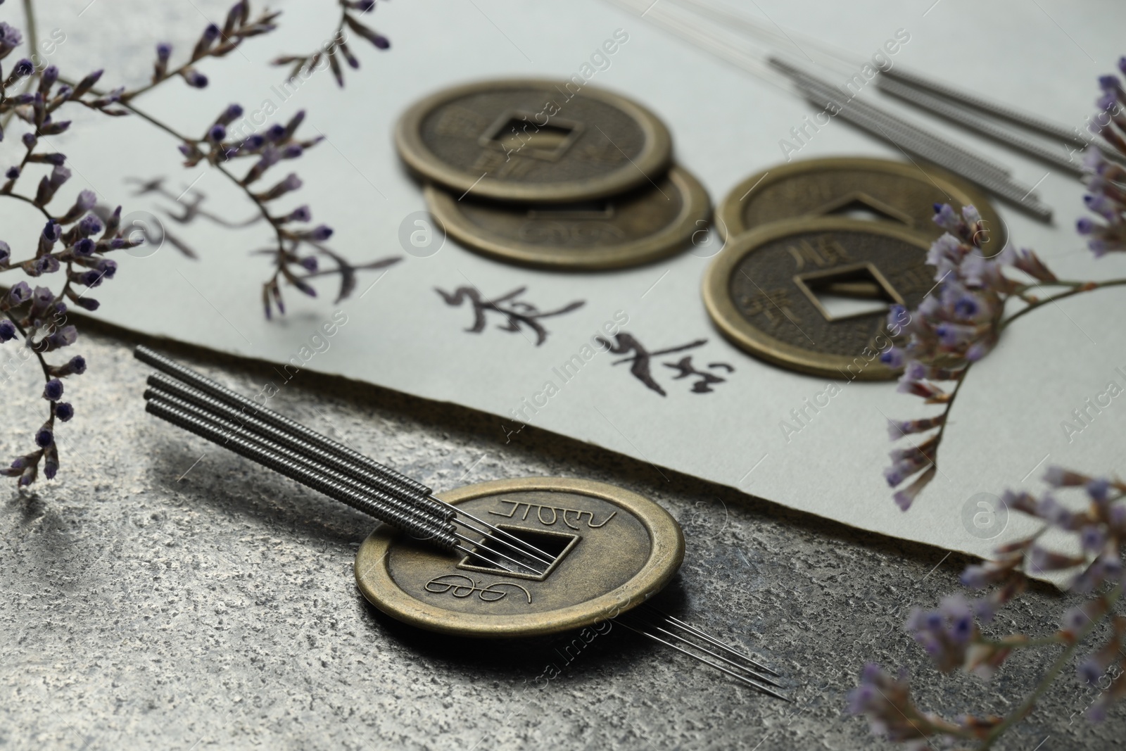 Photo of Acupuncture needles, Chinese coins, flowers and paper with characters on grey textured table, closeup