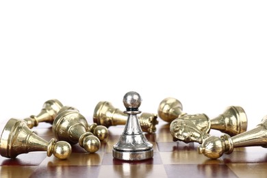 Silver pawn among fallen golden chess pieces on wooden board against white background