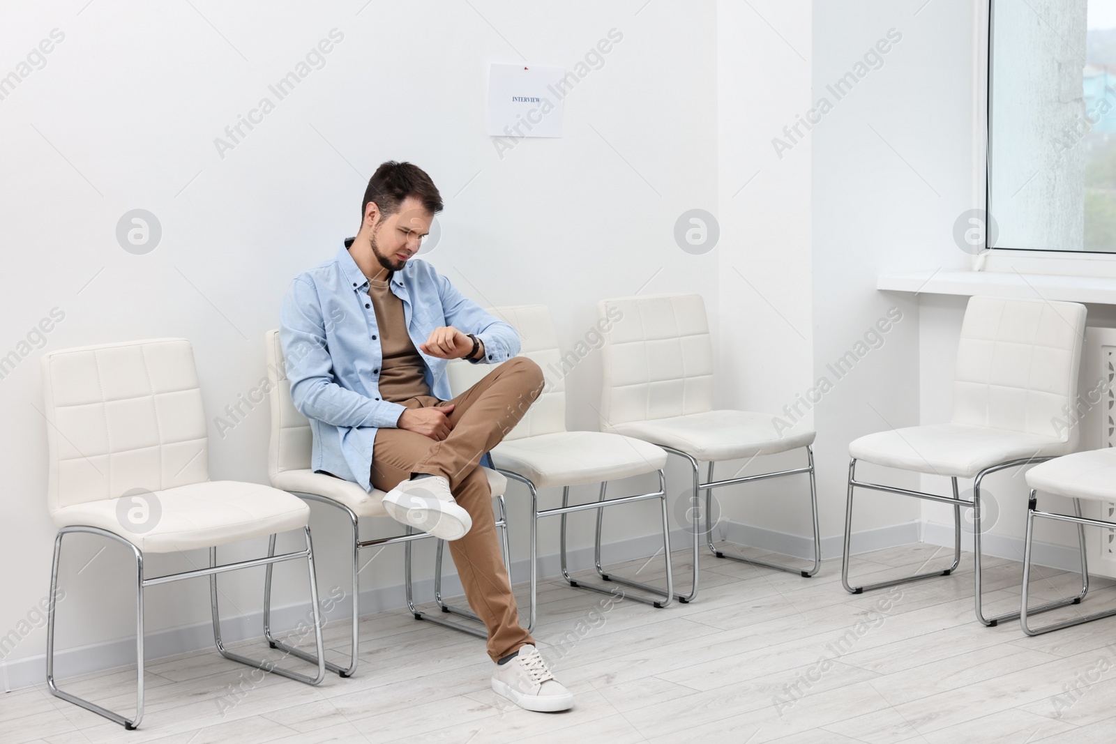 Photo of Man looking at wrist watch and waiting for job interview indoors