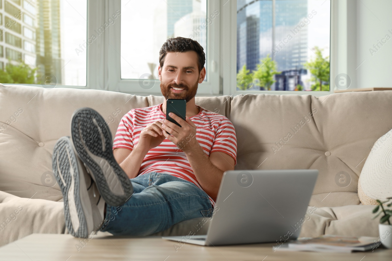 Photo of Handsome man using smartphone on sofa at home