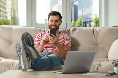 Handsome man using smartphone on sofa at home