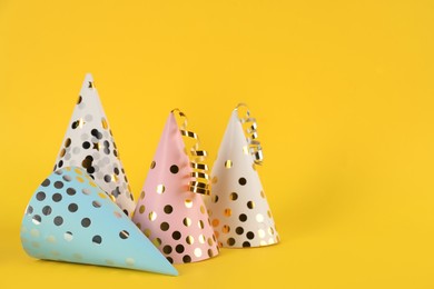 Photo of Bright party hats with streamers on yellow background. Space for text