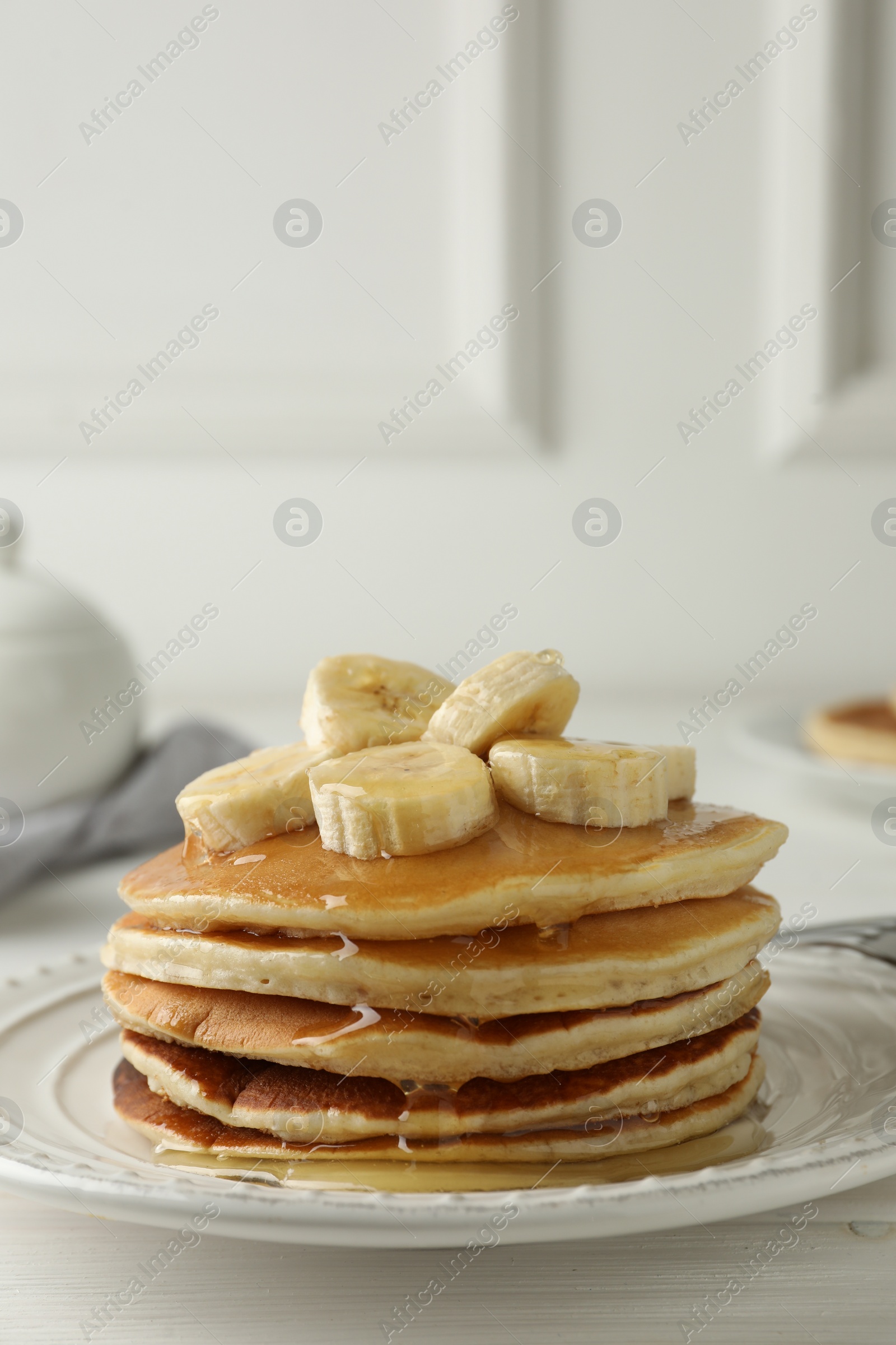 Photo of Delicious pancakes with bananas and honey on white wooden table. Space for text