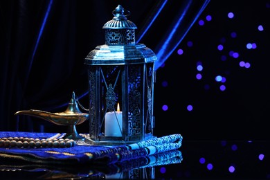 Photo of Arabic lantern, misbaha, Aladdin magic lamp and folded prayer mat on mirror surface against blurred lights at night. Space for text