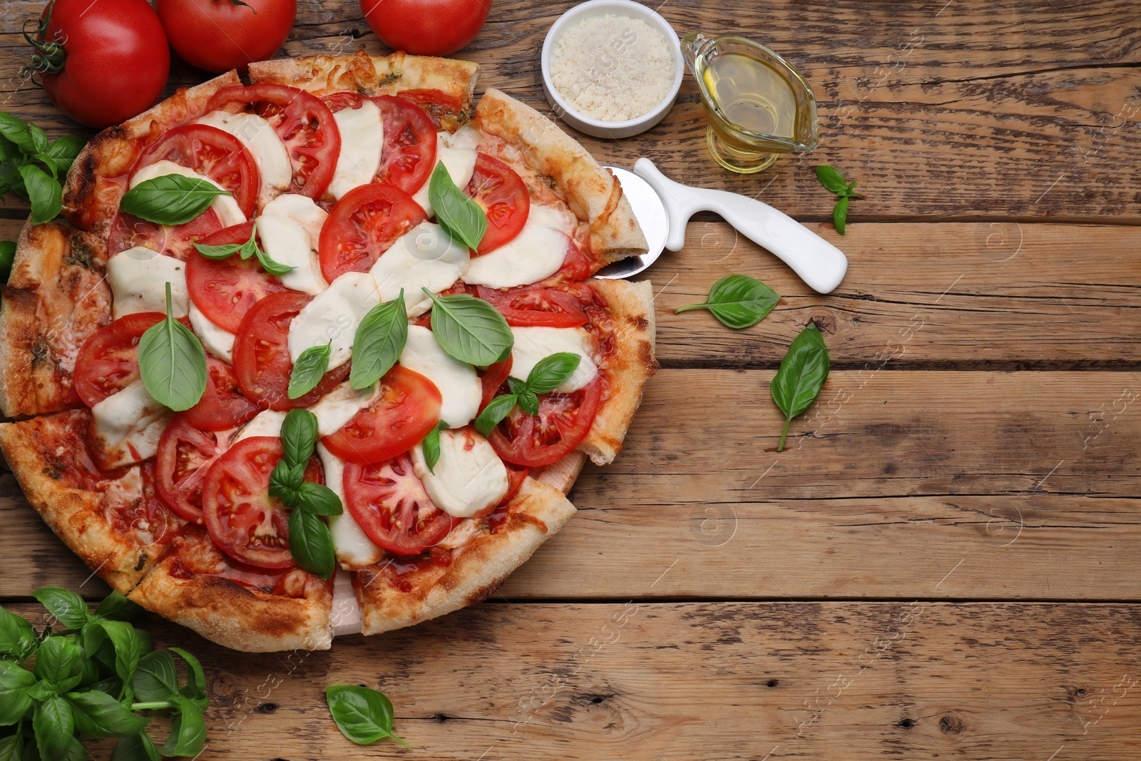 Photo of Delicious Caprese pizza with tomatoes, mozzarella and basil served on wooden table, above view. Space for text