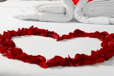 Honeymoon. Heart made with rose petals on bed, closeup