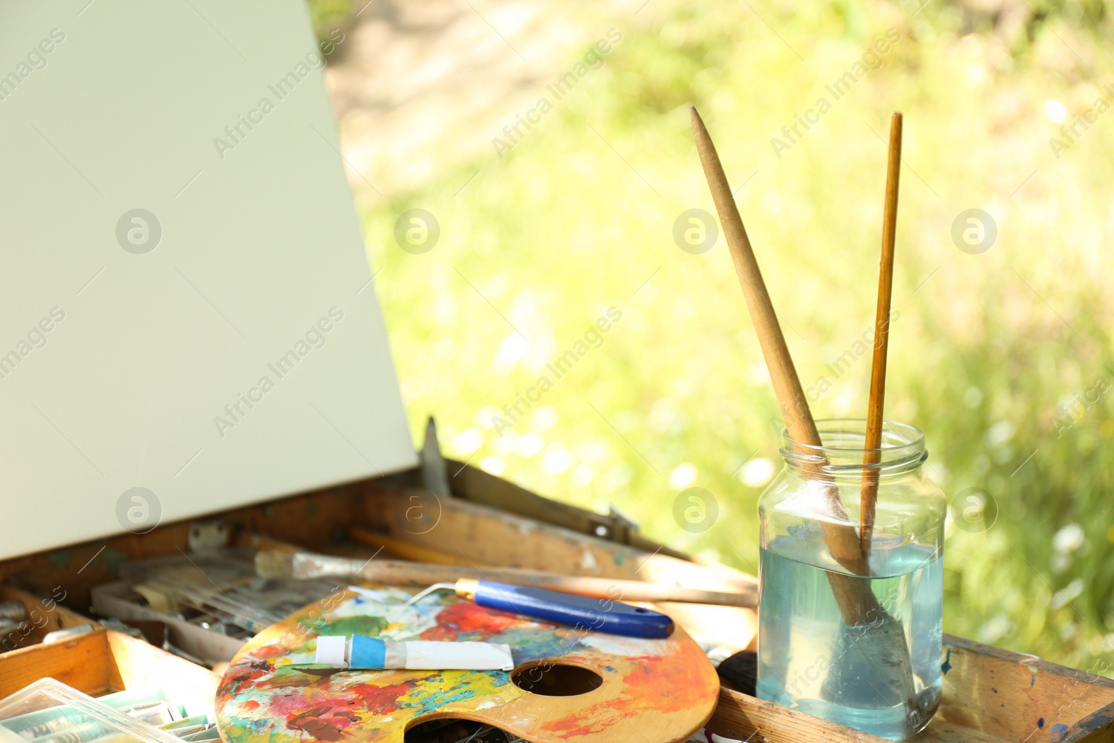 Photo of Easel with canvas and painting equipment outdoors, closeup