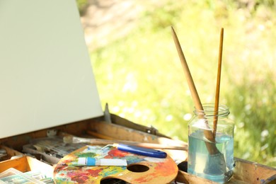 Photo of Easel with canvas and painting equipment outdoors, closeup