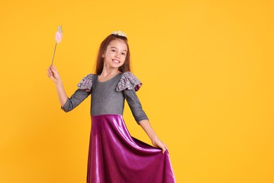 Cute girl in dress with diadem and magic wand on yellow background, space for text. Little princess