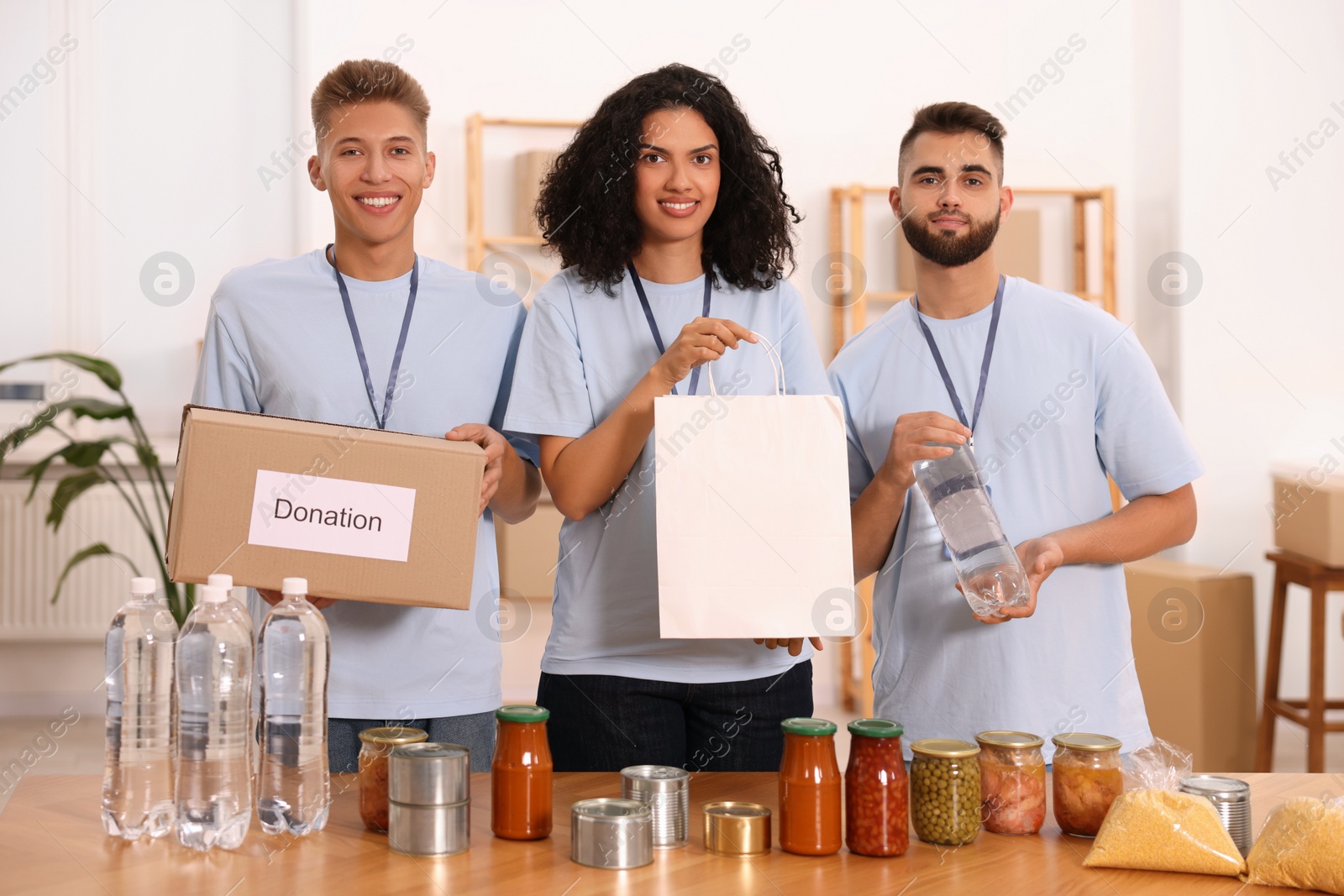 Photo of Portrait of volunteers with donation box, paper bag and food products at table in warehouse