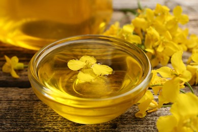Photo of Rapeseed oil in glass bowl and beautiful yellow flowers on wooden table, closeup