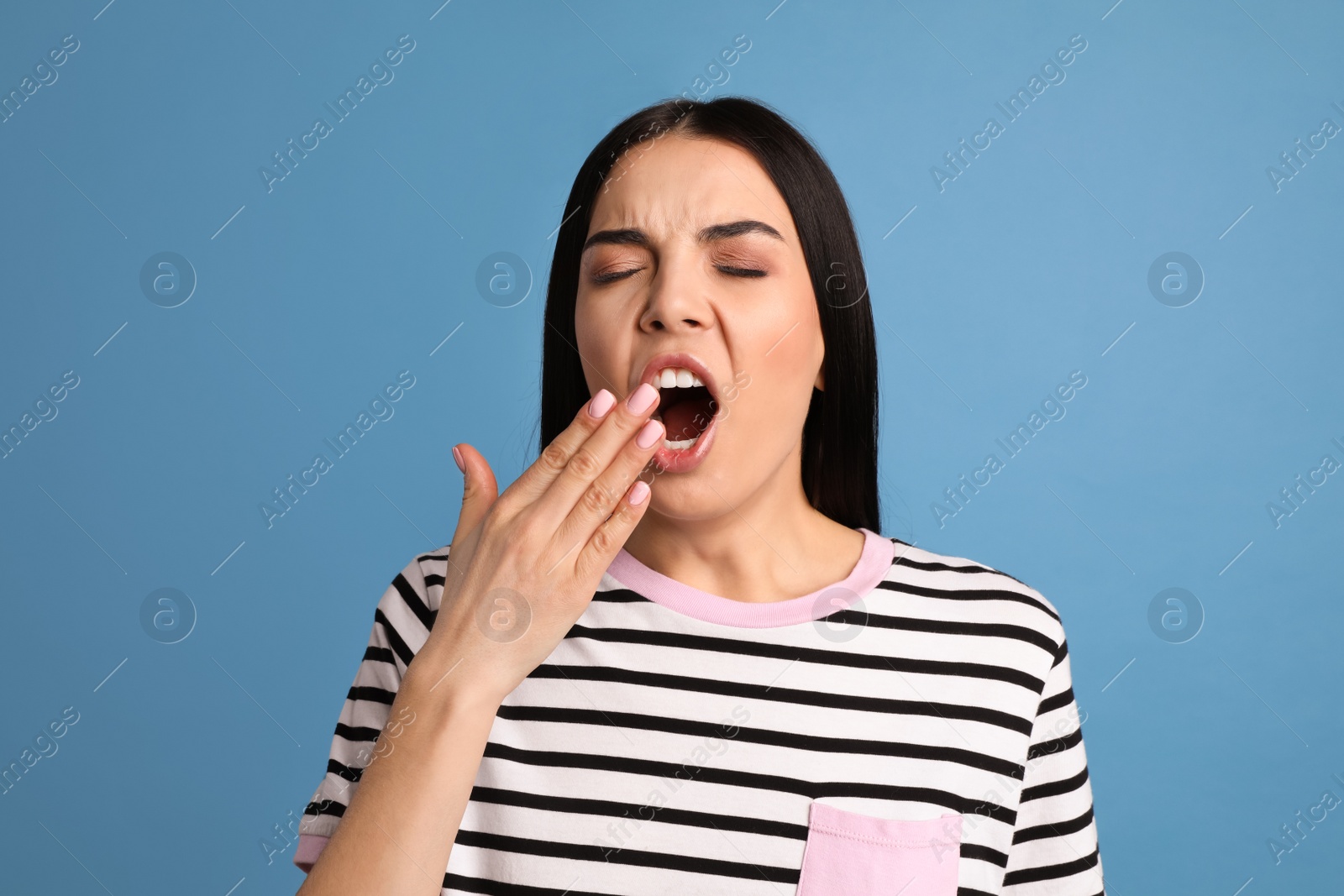 Photo of Young tired woman yawning on light blue background