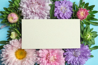 Photo of Beautiful aster flowers with sheet of paper on color background, top view. Space for text