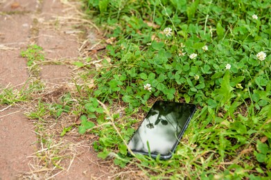 Photo of Smartphone lying on grass near pavement outdoors. Lost and found