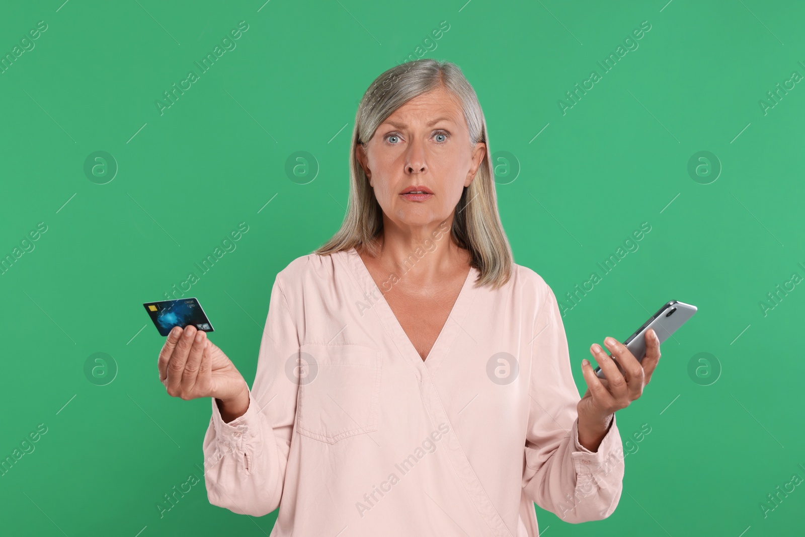 Photo of Worried woman with credit card and smartphone on green background. Be careful - fraud