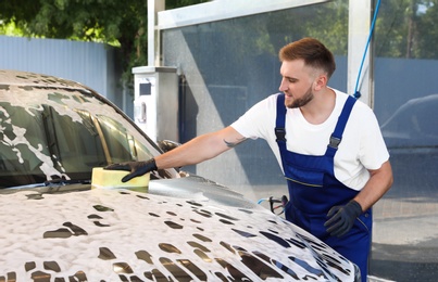 Young worker cleaning automobile with sponge at car wash