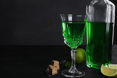 Photo of Absinthe, spoon, brown sugar and lime on black table, space for text. Alcoholic drink