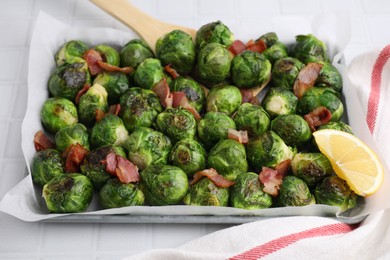 Photo of Delicious roasted Brussels sprouts, bacon and lemon in baking dish on white tiled table