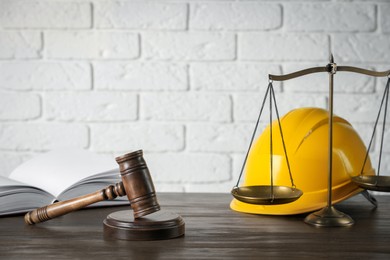 Labour, construction and land law concepts. Judge gavel, scales of justice, open book with protective helmet on wooden table