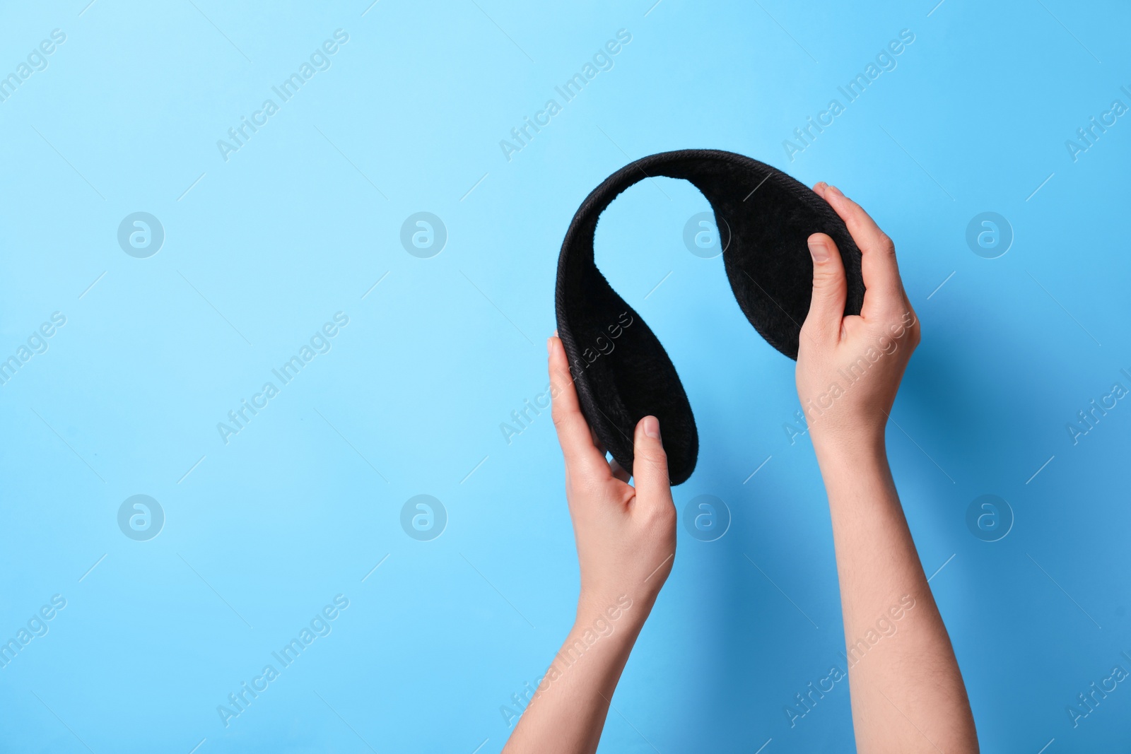 Photo of Woman holding stylish winter earmuffs on light blue background, closeup. Space for text