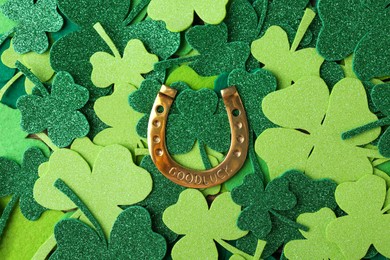 Photo of St. Patrick's day. Golden horseshoe on green decorative clover leaves, top view