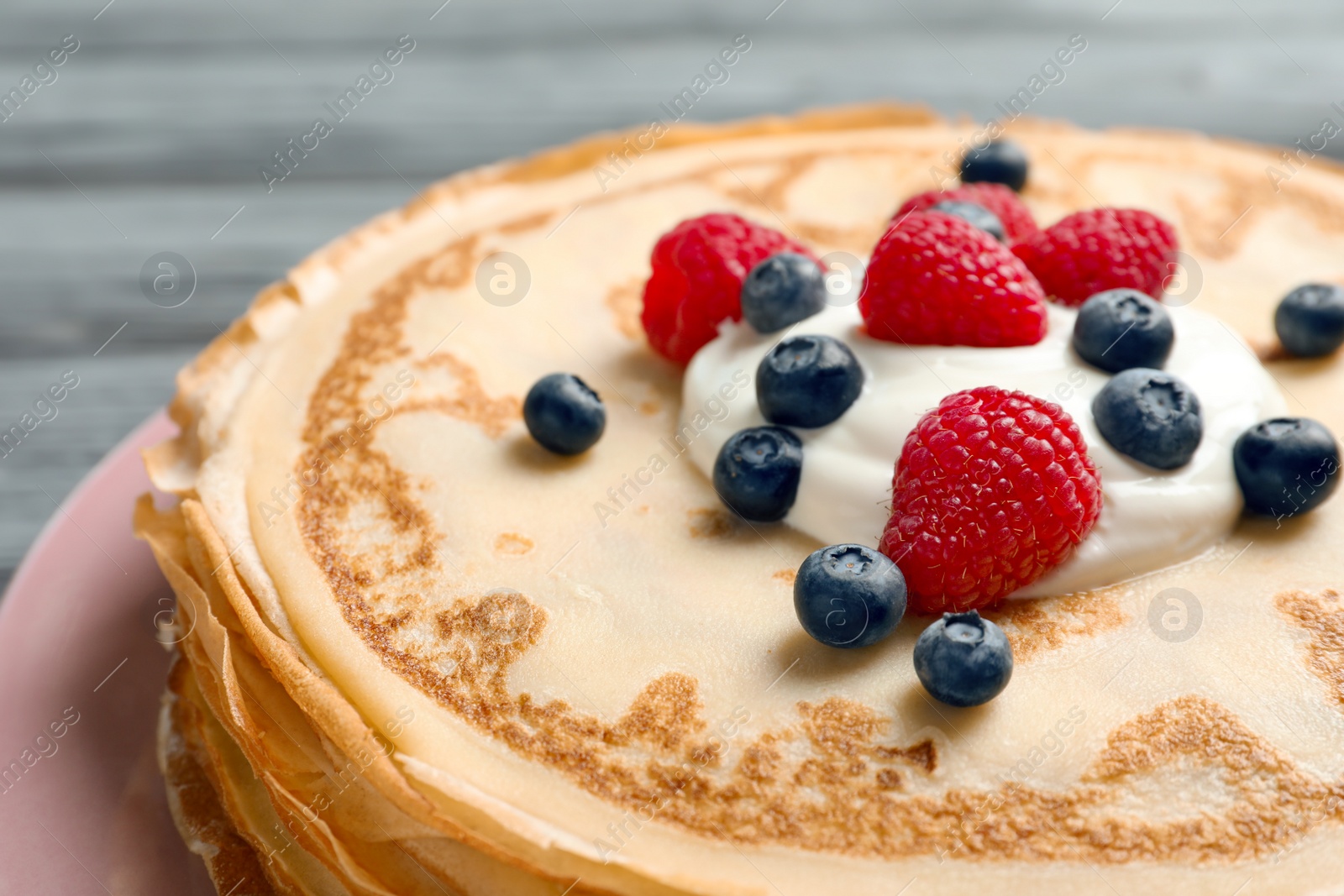 Photo of Thin pancakes served with cream and berries on plate, closeup