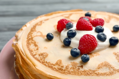 Photo of Thin pancakes served with cream and berries on plate, closeup