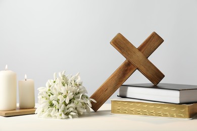 Photo of Burning church candles, wooden cross, ecclesiastical books and flowers on white table