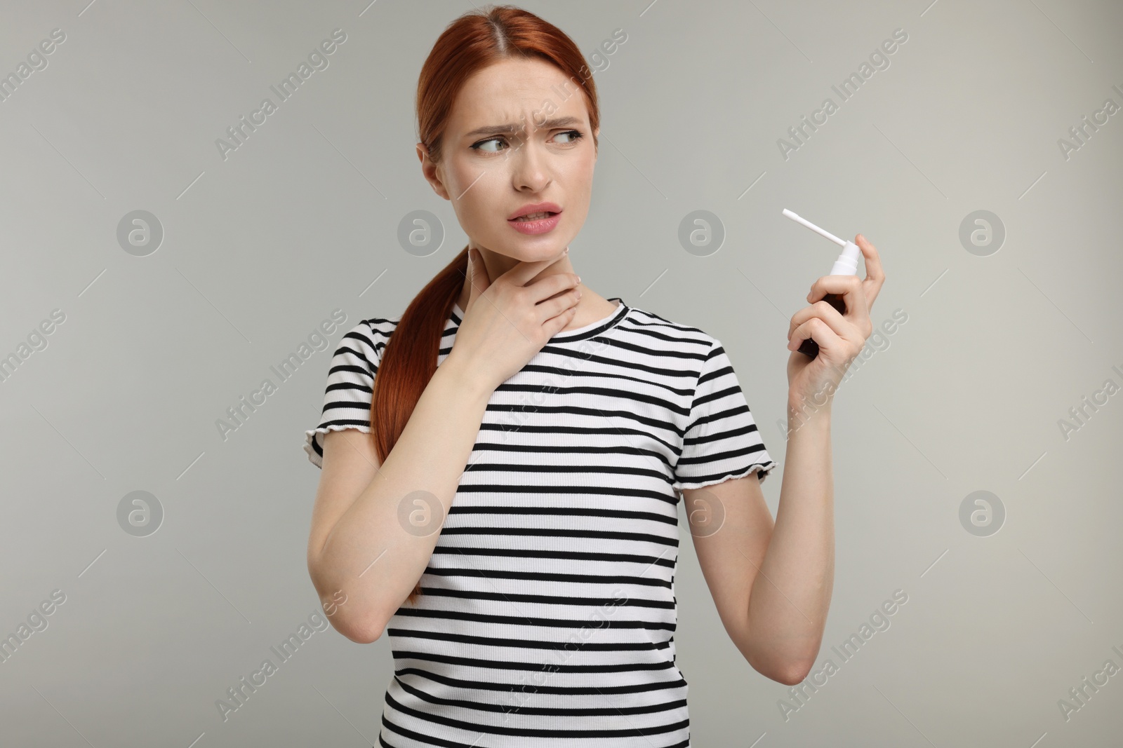 Photo of Young woman holding throat spray on grey background