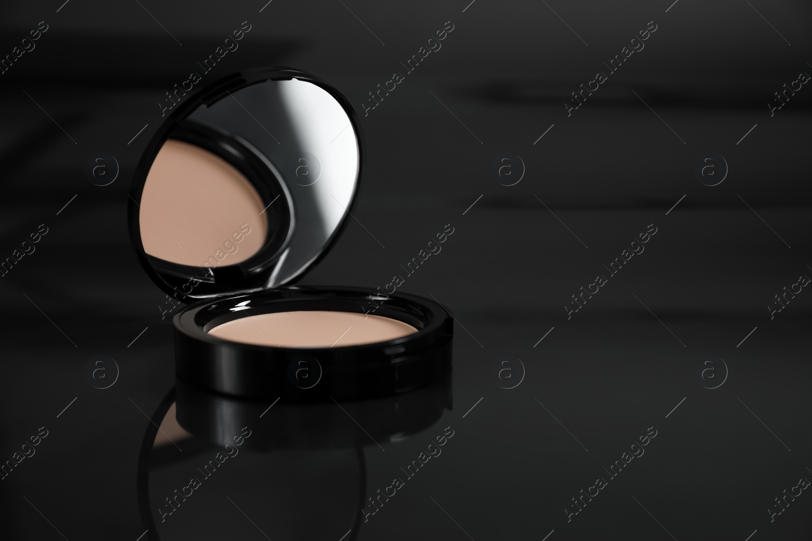 Photo of Open face powder on black mirror surface, closeup. Space for text