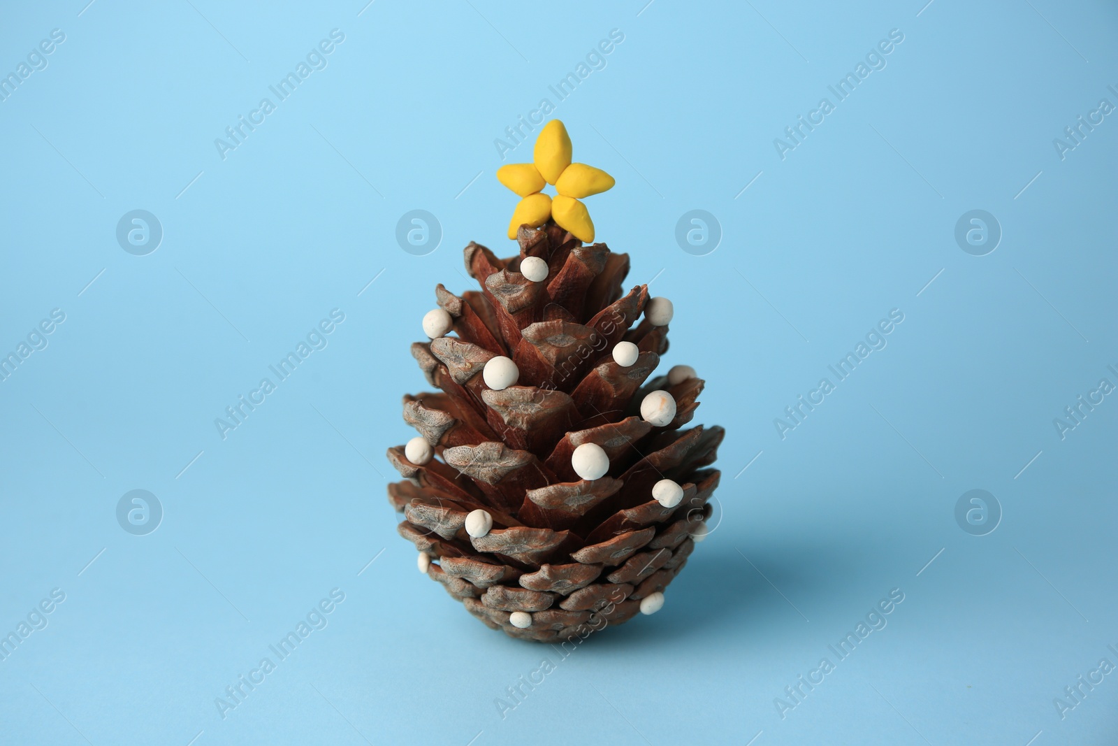 Photo of Christmas tree made from pine cone and plasticine on light blue background. Children's handmade ideas