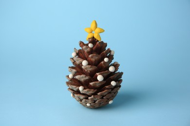 Photo of Christmas tree made from pine cone and plasticine on light blue background. Children's handmade ideas