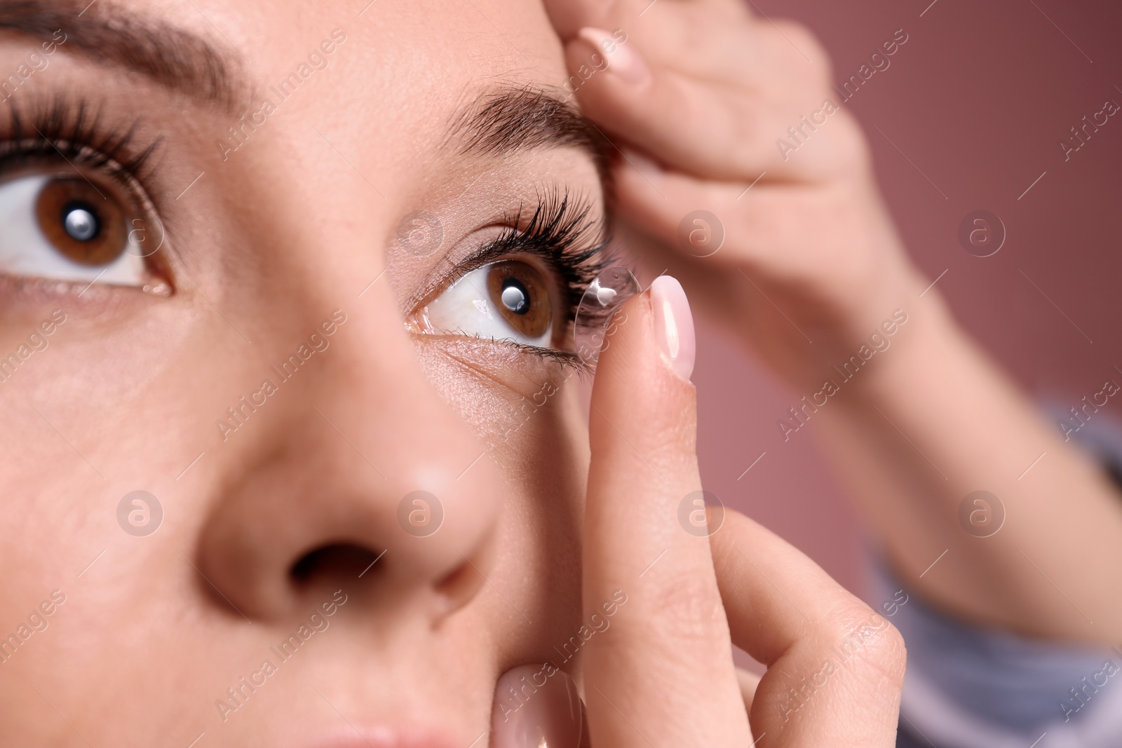 Photo of Young woman putting contact lens in her eye on color background