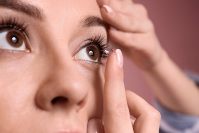 Photo of Young woman putting contact lens in her eye on color background